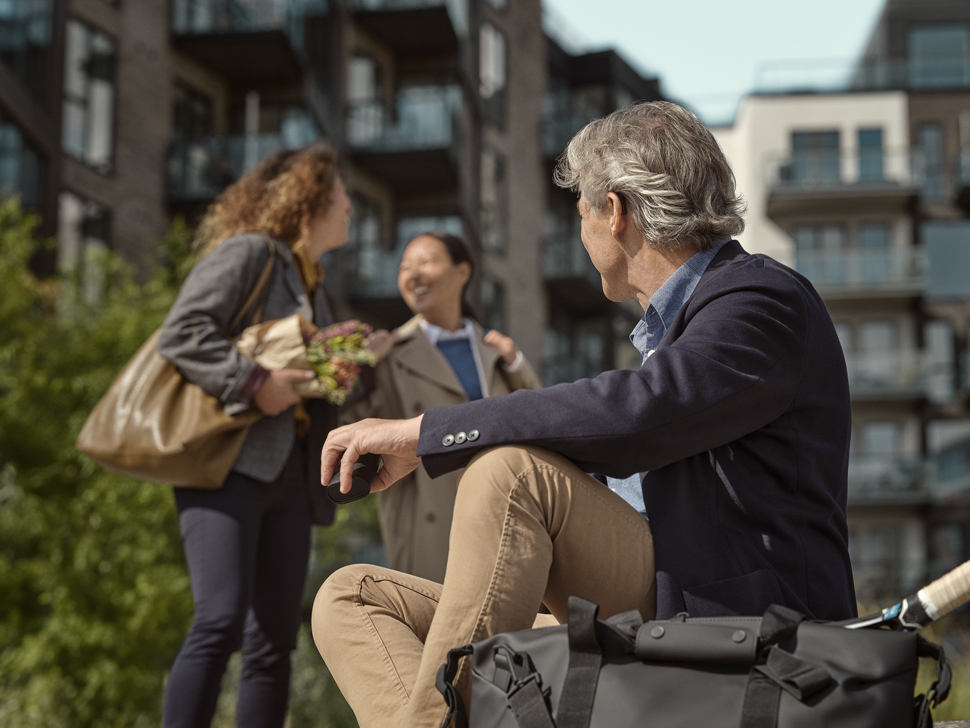Man sitting outside wearing Widex SmartRIC hearing aids while listening to people talking .
