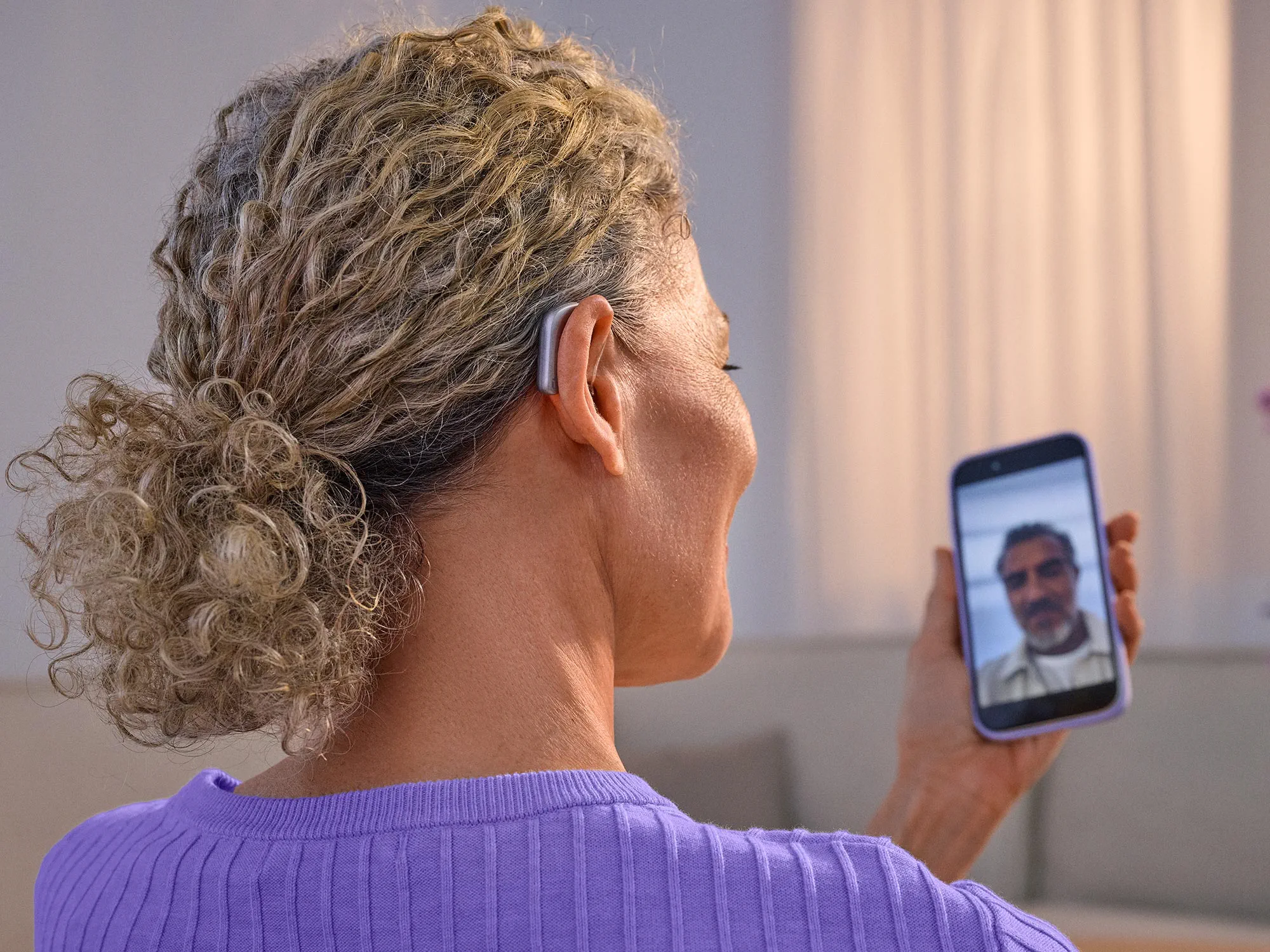 Woman on the phone facetiming with a friend wearing Widex Smart RIC hearing aids getting the sound directly from phone to hearing aids.