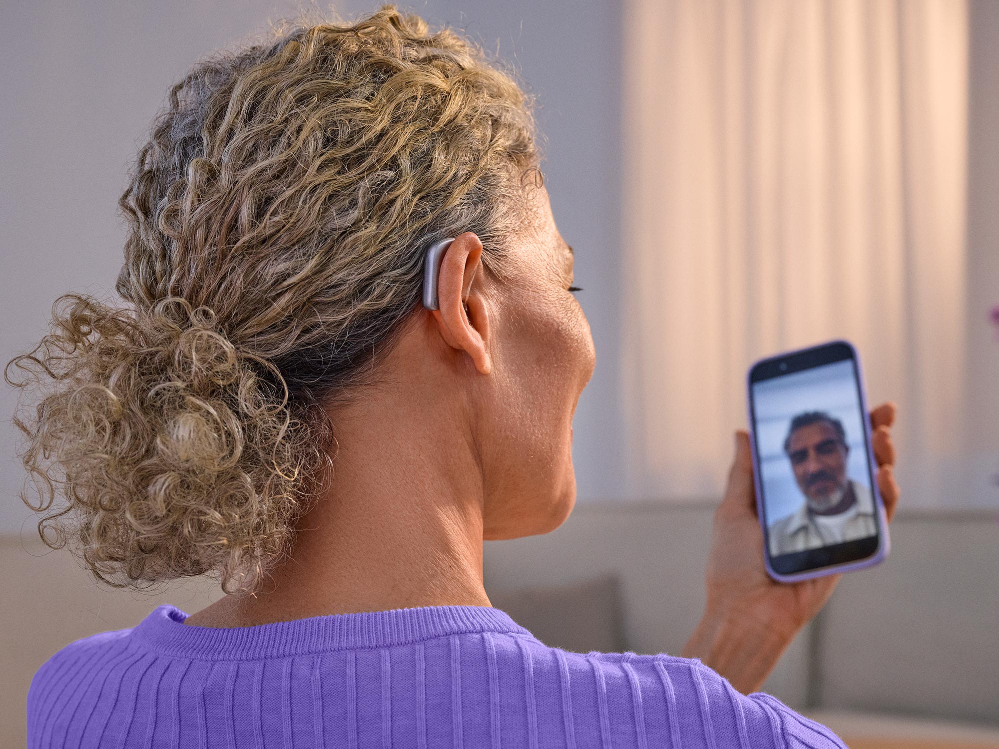 Woman on the phone facetiming with a friend wearing Widex Smart RIC hearing aids getting the sound directly from phone to hearing aids.