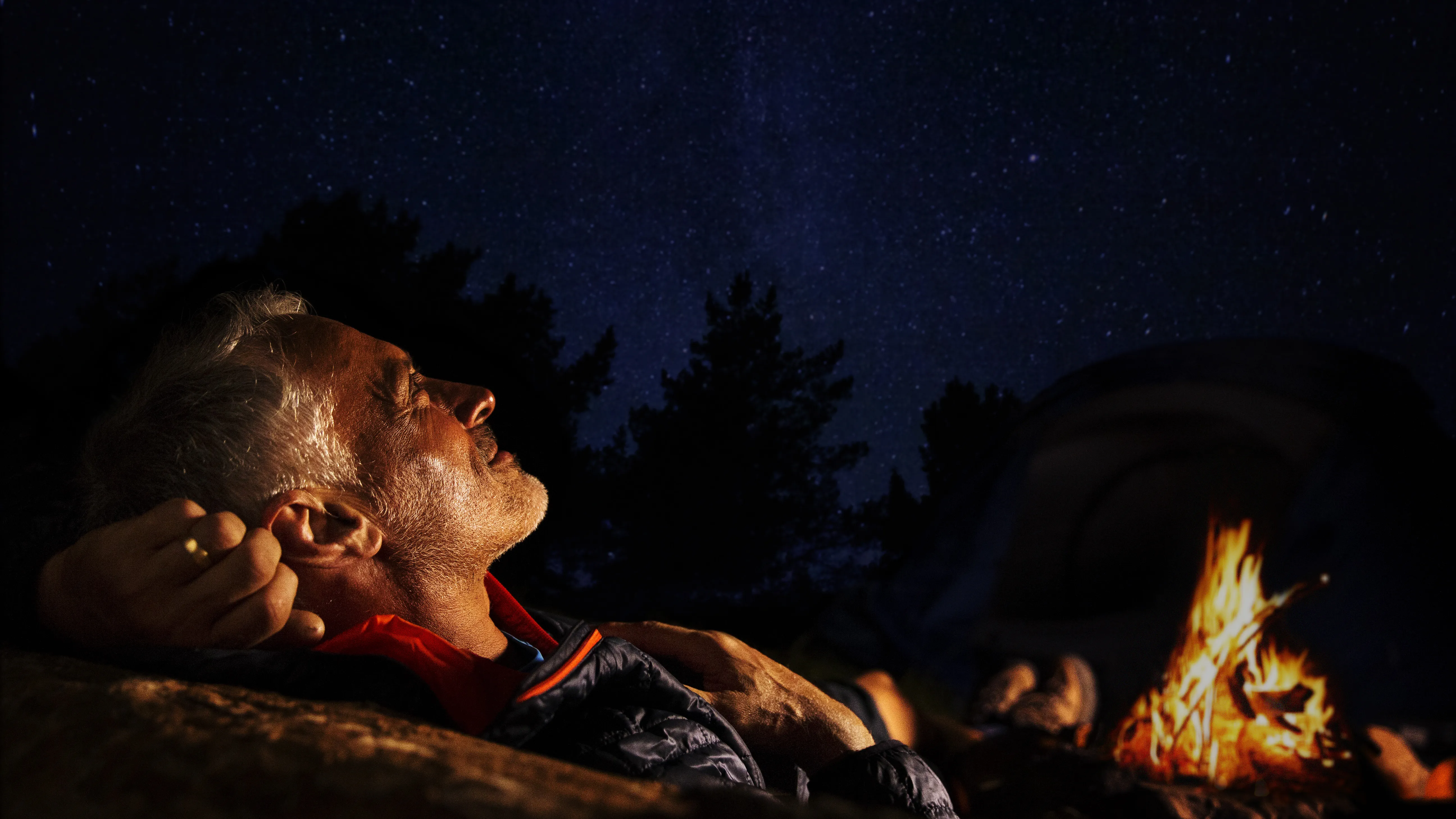 Man at a forest bonfire, having difficulty hearing conversations because of hearing loss.