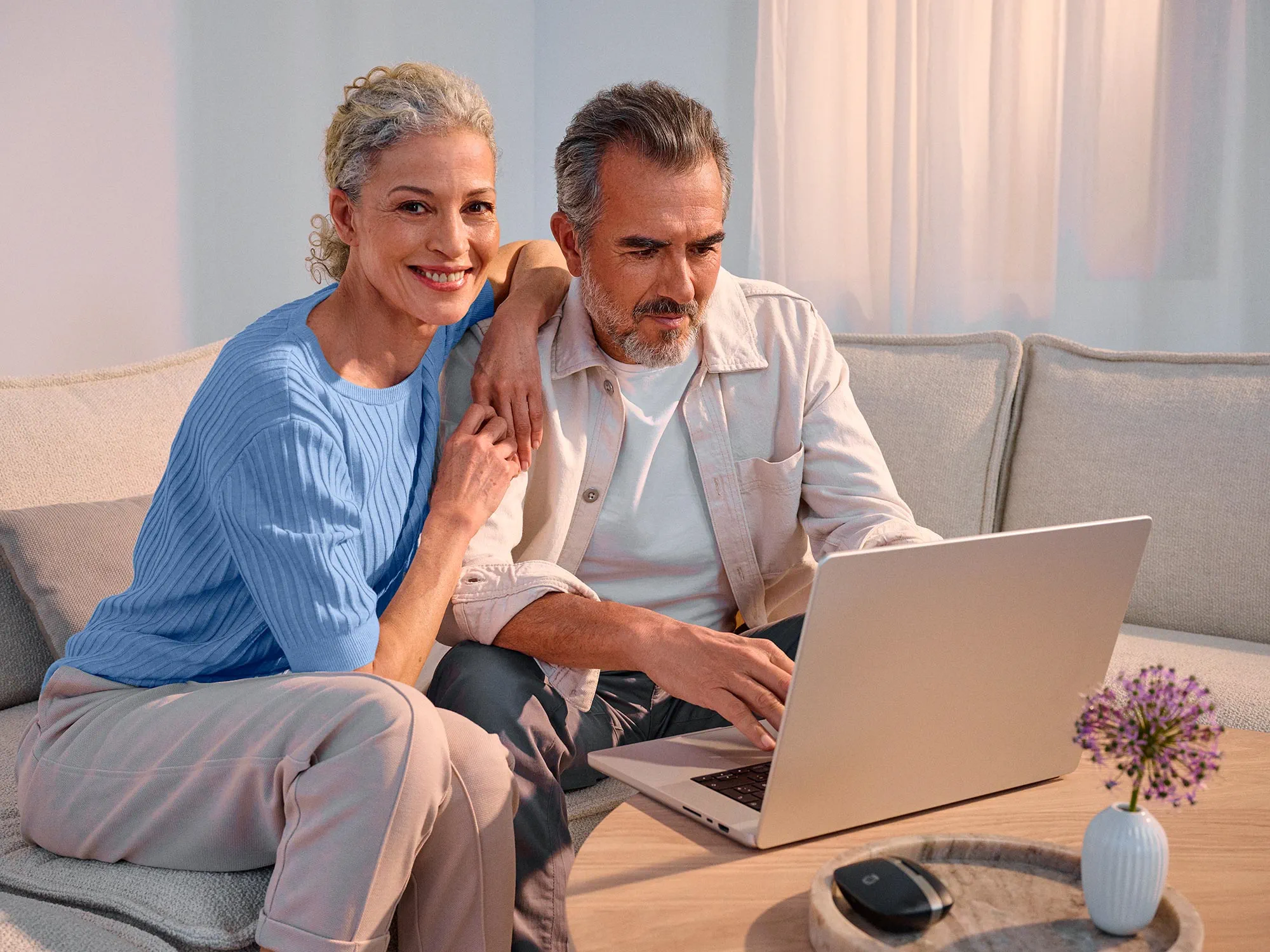 Hopeful couple with technology, both wearing hearing aids.