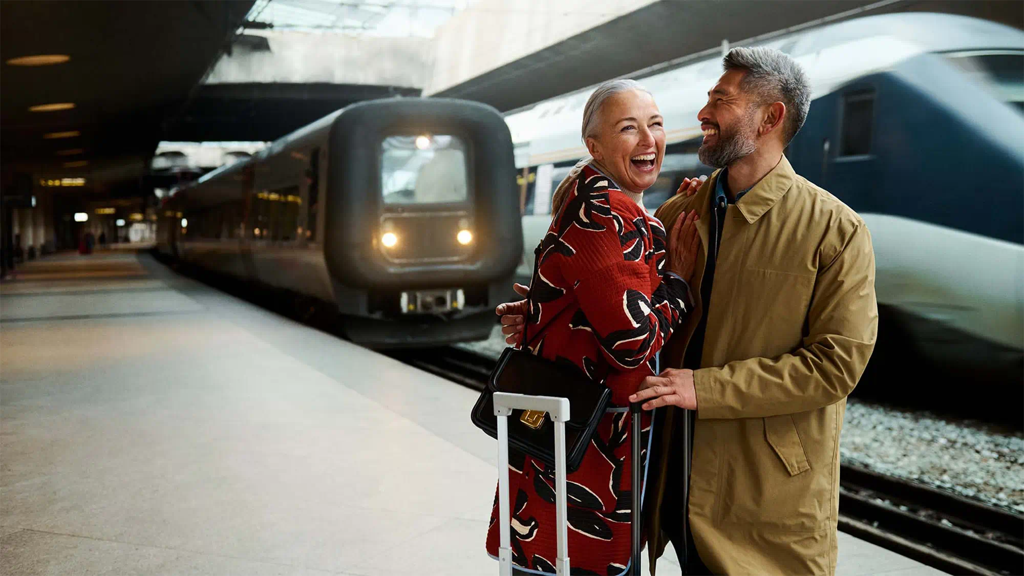 Woman with hearing-loss traveling confidently with hearing-aids, supported by a friend at a busy train station platform.