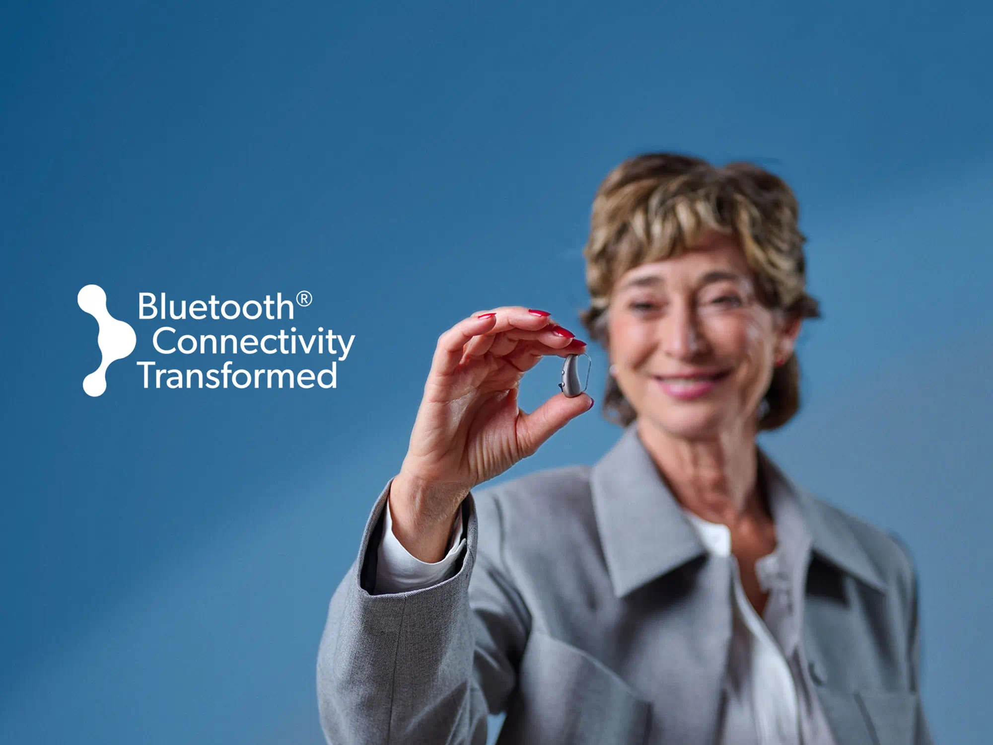 Person with hearing-loss holding a Bluetooth-enabled hearing-aid device, showcasing advanced connectivity and compact design.
