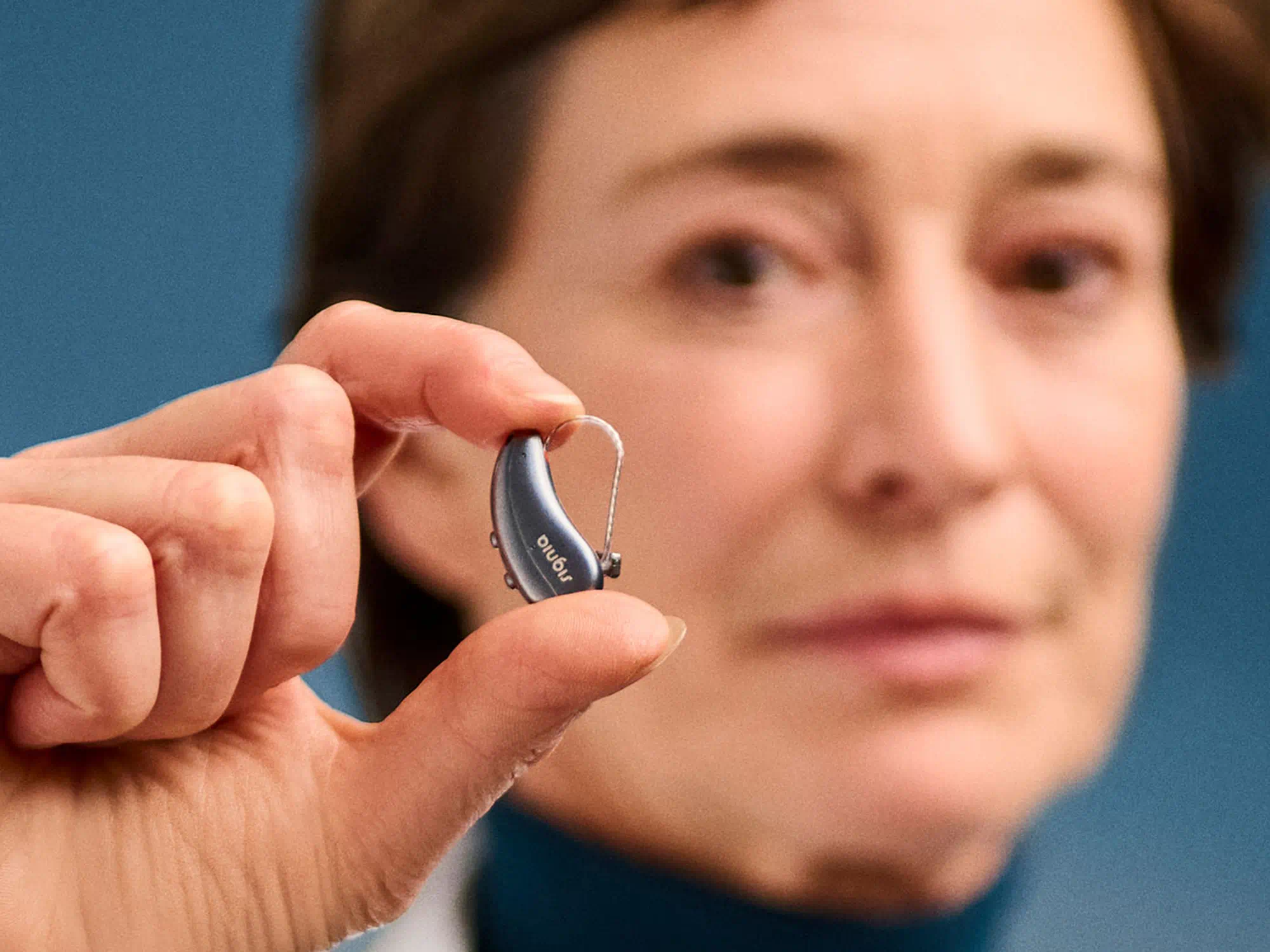 Hand holding a tiny hearing-aid against a blue background, emphasizing discreet solutions for people with hearing-loss.