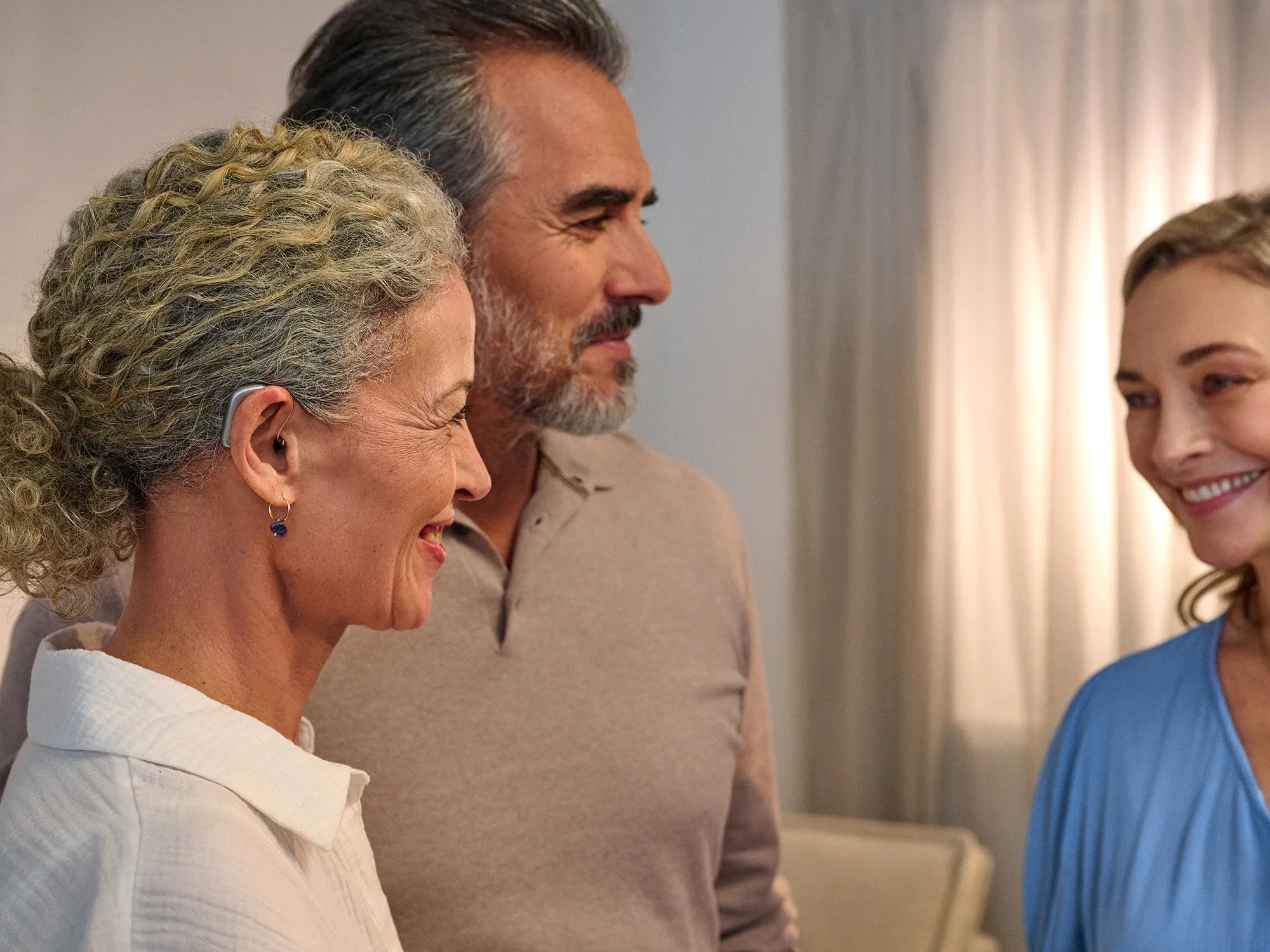 Couple chatting to friend while woman is wearing Widex Smart RIC hearing aids enjoying she can her the converstation