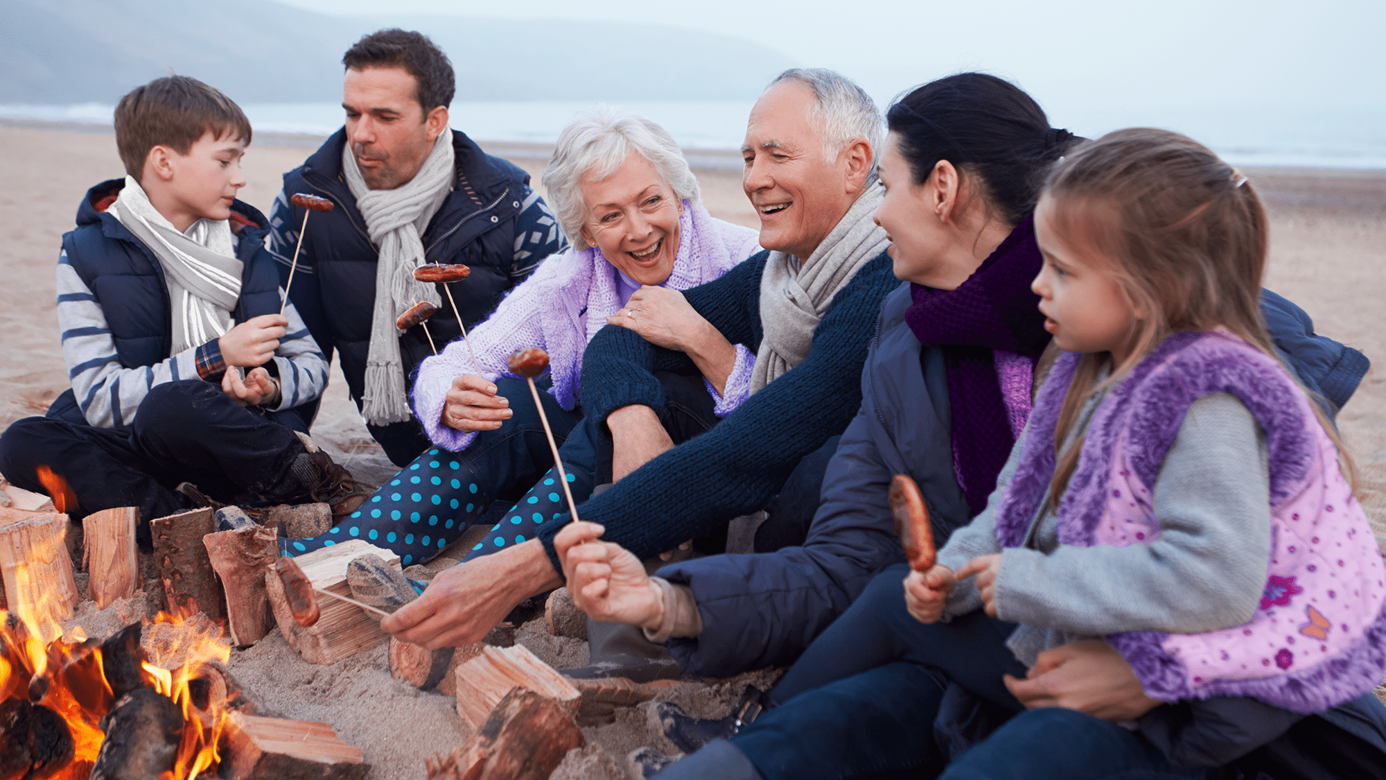 Family in winter gear around a beach campfire, illustrating cold-weather hearing aid care.