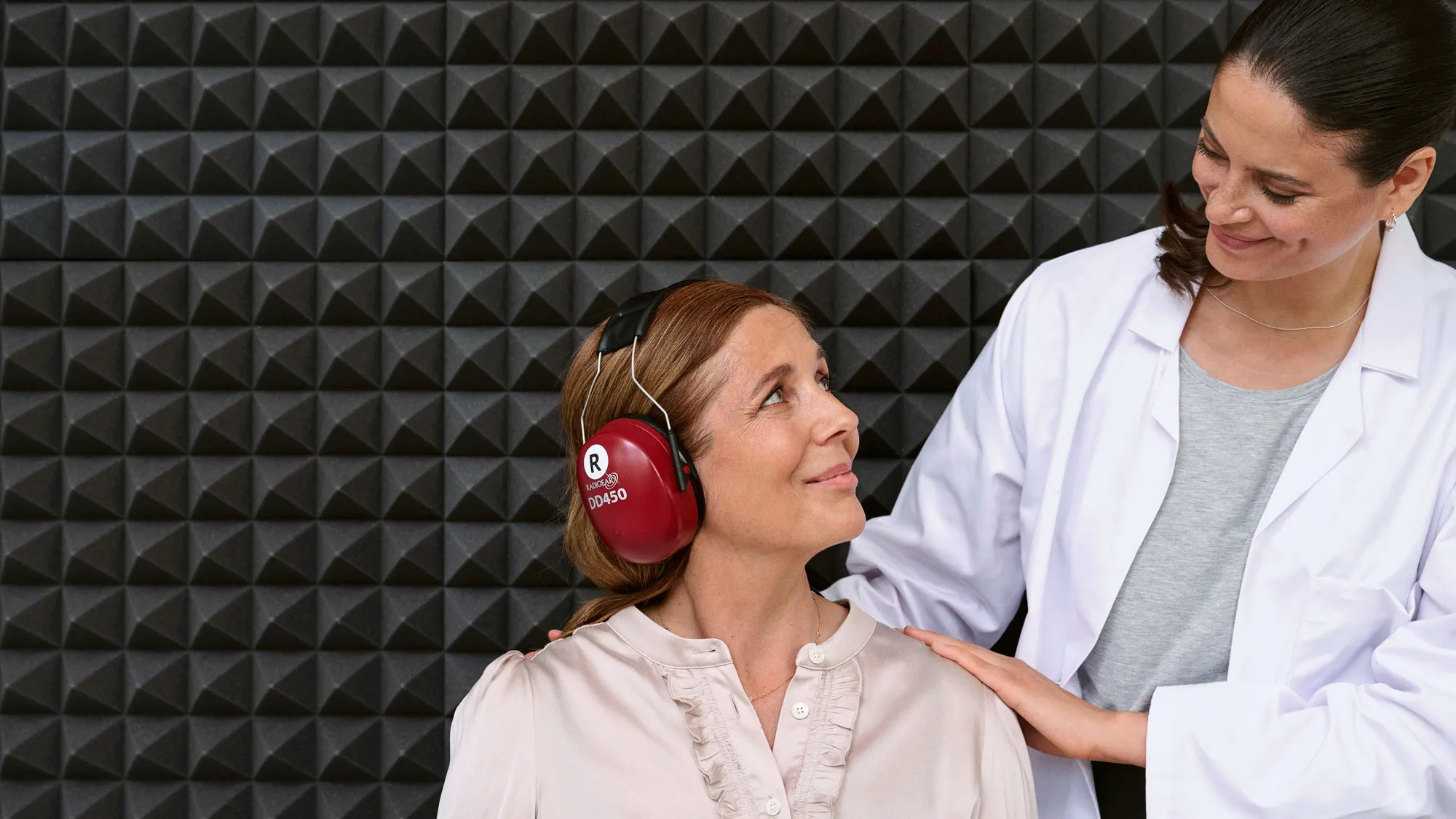 Início de um teste auditivo numa cabine acústica, com o cliente e o especialista a preparar-se para o teste.