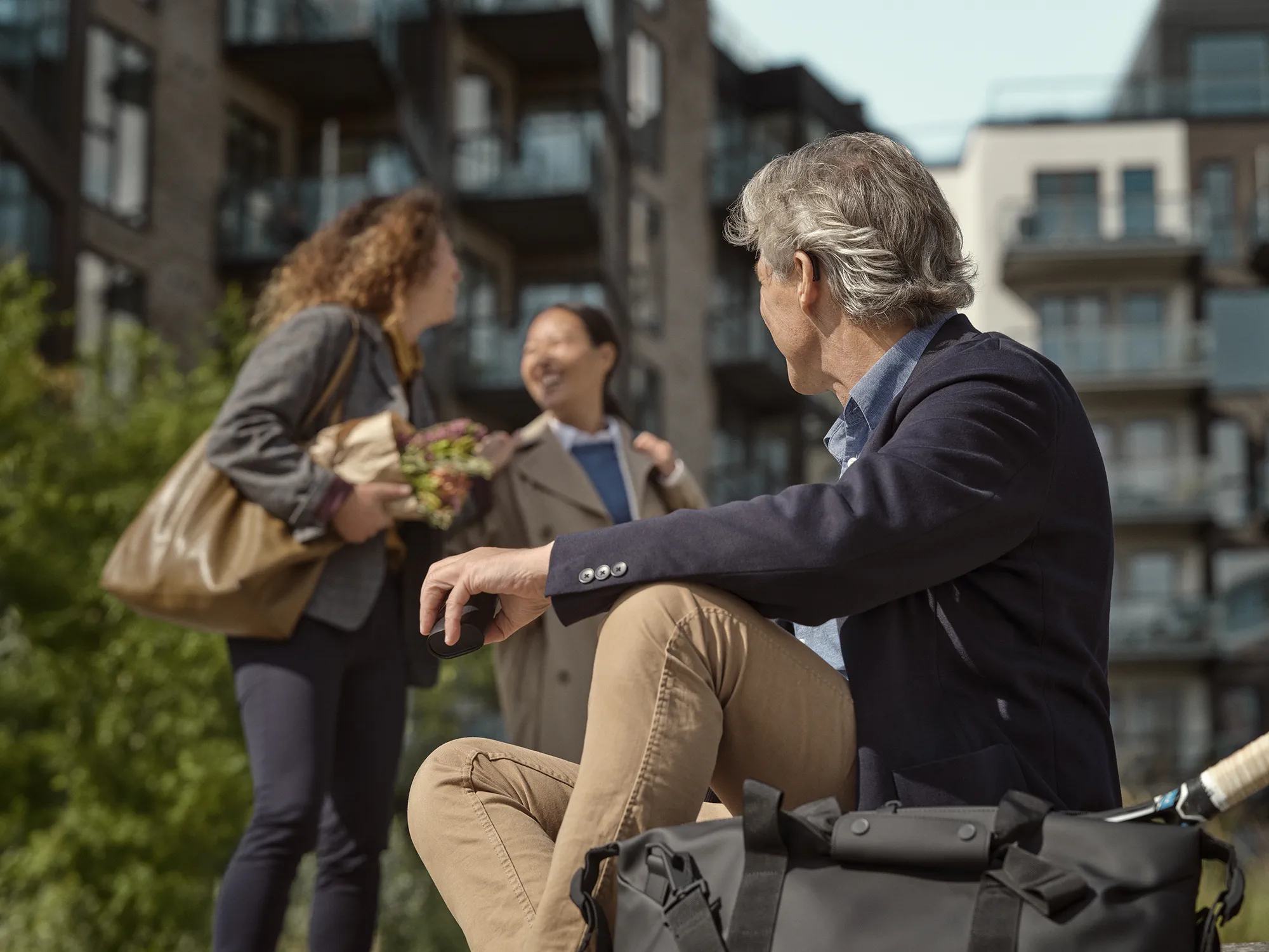 Man sitting outside wearing Widex SmartRIC hearing aids while listening to people talking .