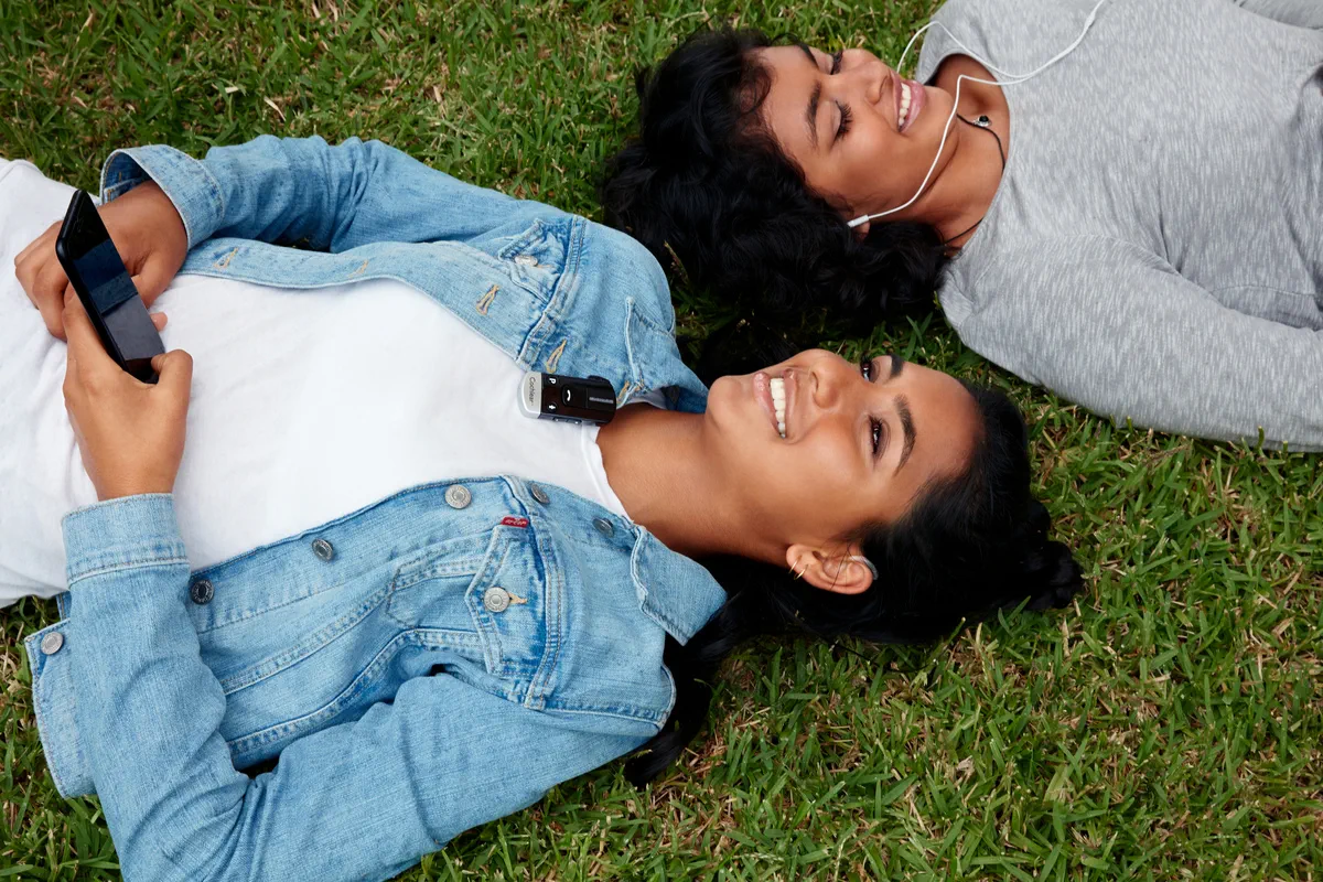 Women wearing Cochlear Implants relaxing in the grass hearing better with Cochlear wireless accessories.