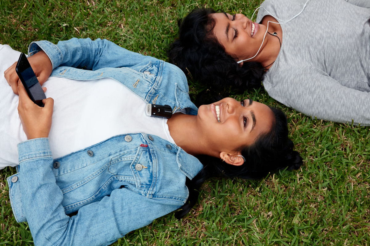Women wearing Cochlear Implants relaxing in the grass hearing better with Cochlear wireless accessories.